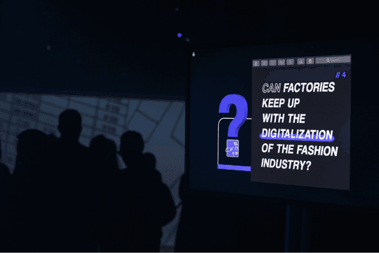 The projection displaying "CAN FACTORIES KEEP UP WITH THE DIGITALIZATION OF THE FASHION INDUSTRY?" over a large question mark, visitors silhouetted in front.