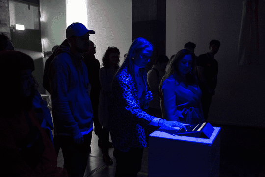 A visitor making a choice on the tablet interface, blue-lit, small crowd gathered around.
