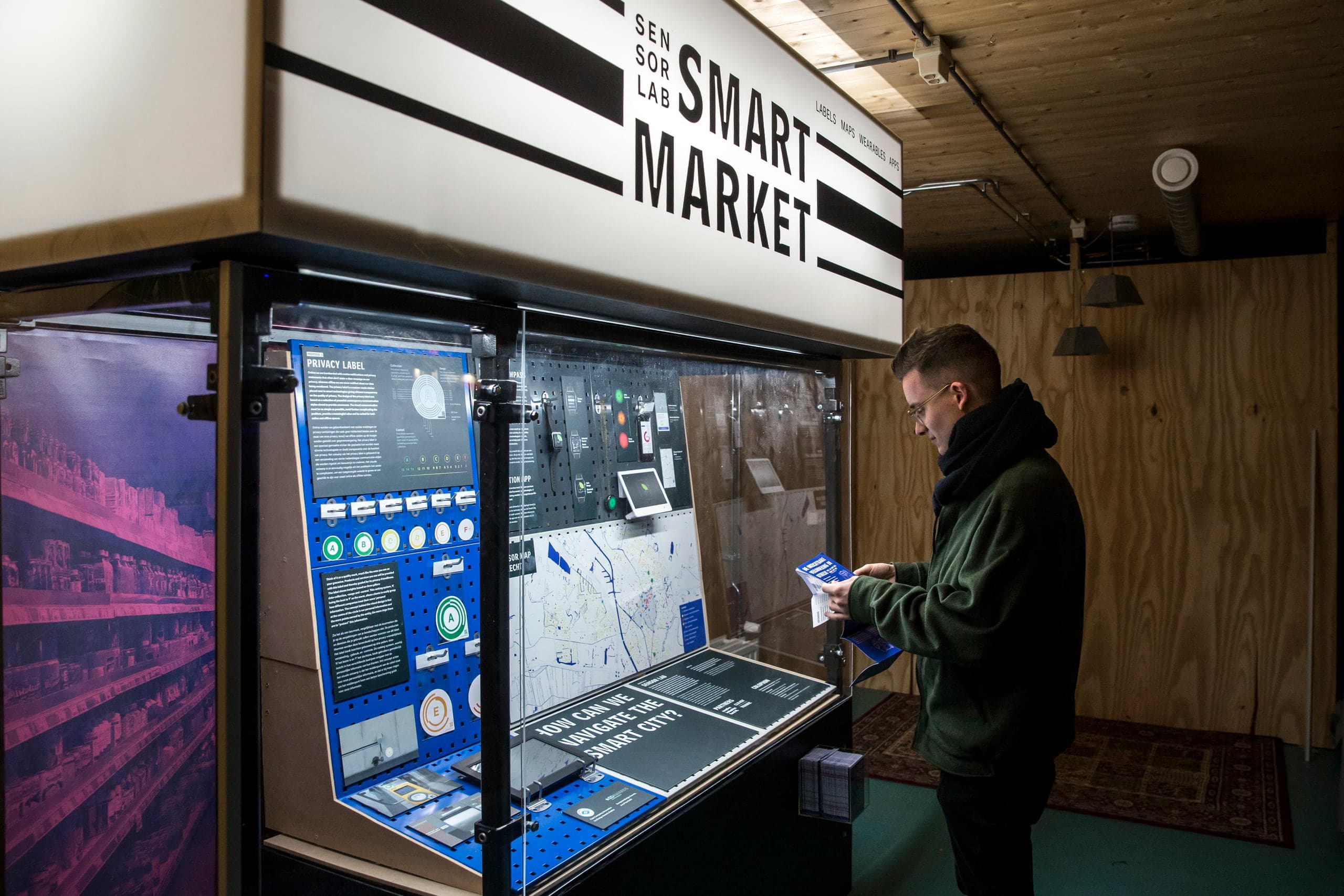 The Smart Market kiosk at RAUM, Utrecht: a visitor reading the "Privacy Label" panel, a pink-toned city photograph on the left wall. Photo by Thijs Rooimans.
