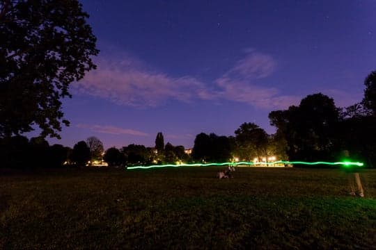 A dusk shot: the green signal trail curves through a park beneath a fading blue sky.